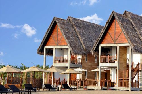 An outdoor daytime view of Maalu Maalu Resort & Spa featuring traditional wooden chalets with thatched roofs, sun loungers, and beach umbrellas along the coast in Pasikuda, Sri Lanka