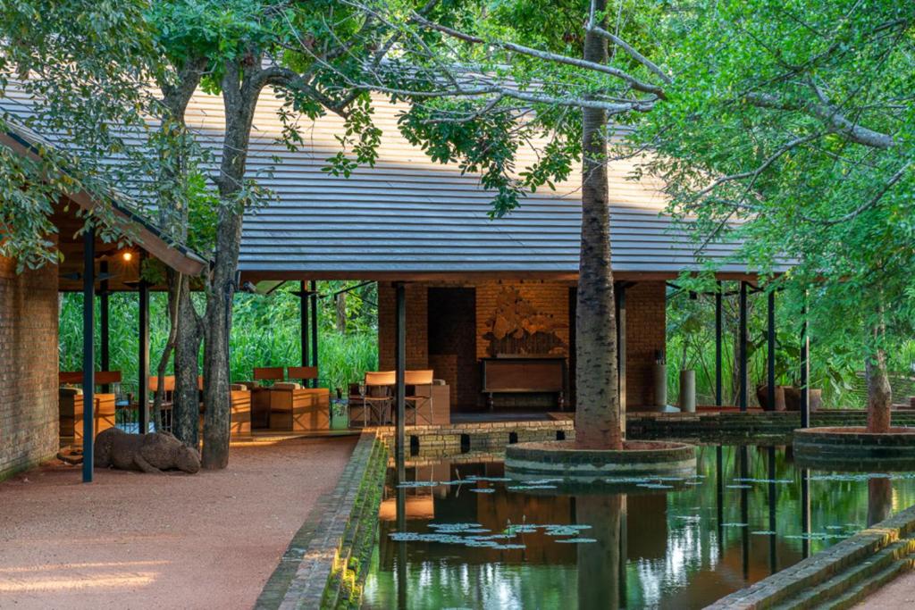 An outdoor daytime view of Taru Villas featuring a pavilion-style resort building with a pitched roof, an open-air veranda, a reflecting pool with water lilies, and surrounding mature trees in Sri Lanka