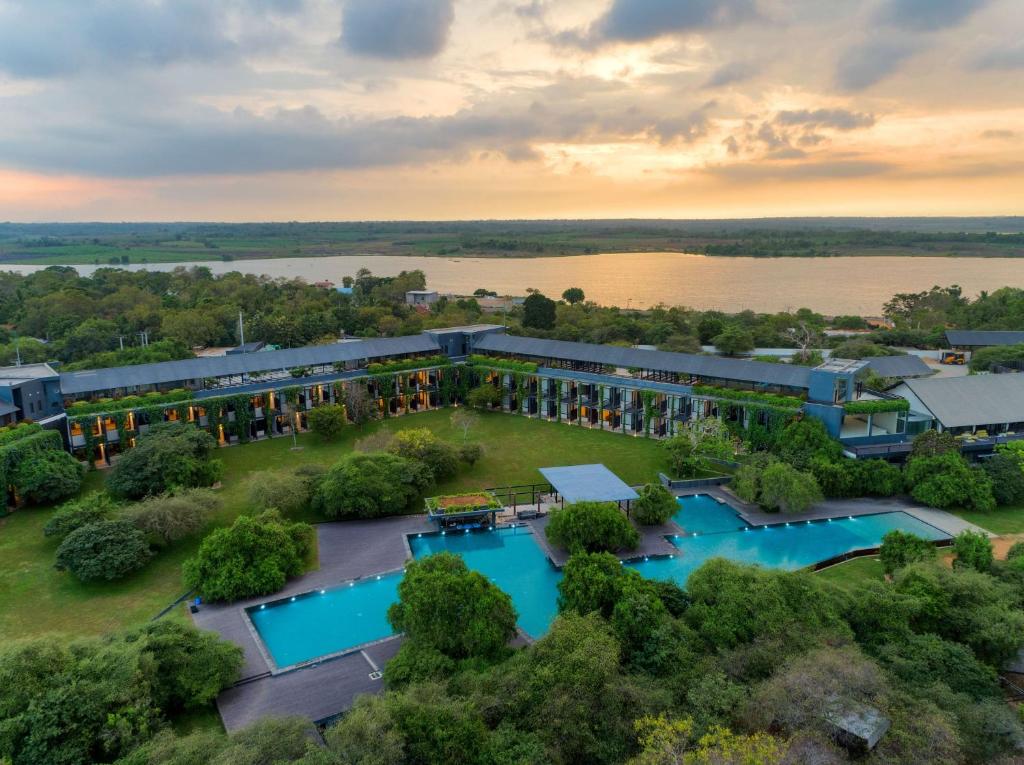 An outdoor aerial twilight view of the DoubleTree by Hilton resort featuring a large swimming pool, modern architecture, and surrounding trees overlooking a lake at sunset in Yala, Sri Lanka