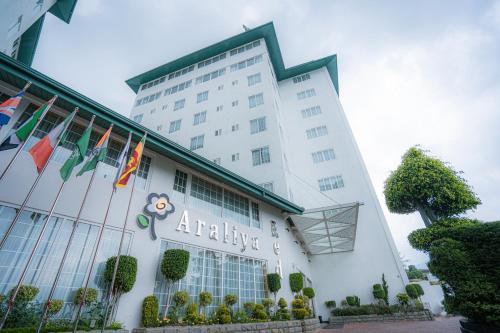 An outdoor low-angle daytime view of the modern Araliya hotel building featuring tall white architecture, a row of international flags, and manicured landscaping under a cloudy sky in Sri Lanka