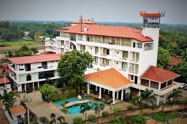 An outdoor elevated daytime view of Valampuri hotel featuring multi-story white architecture with orange-tiled pitched roofs, a swimming pool, and surrounding green landscape in Sri Lanka