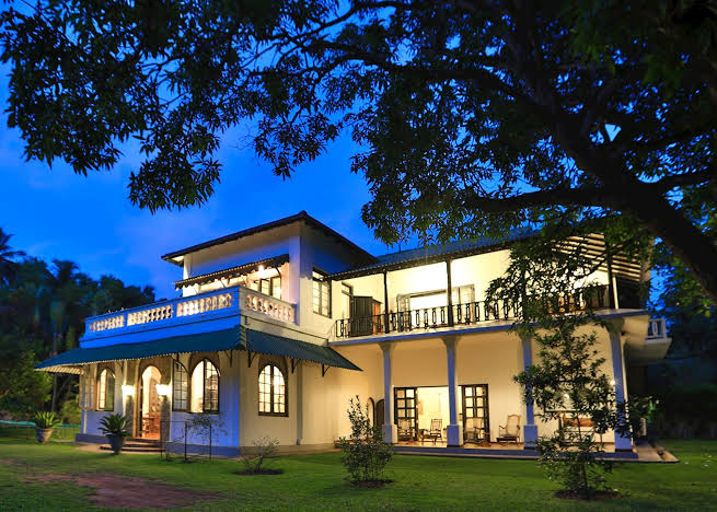 An outdoor twilight view of Horathapola Estate featuring the illuminated facade of the restored 19th-century colonial plantation bungalow set within a working coconut estate in Pannala, Sri Lanka