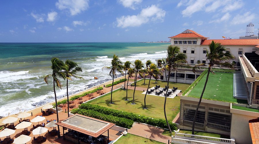 An outdoor high-angle daytime view of Galle Face Hotel in Colombo, featuring a historic colonial seafront architecture, manicured lawns, palm trees, and the ocean view in Sri Lanka