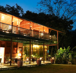 An outdoor twilight view of Planter's Bungalow, a peaceful nature retreat featuring warm lighting, traditional architecture, and surrounding greenery in Ella, Sri Lanka